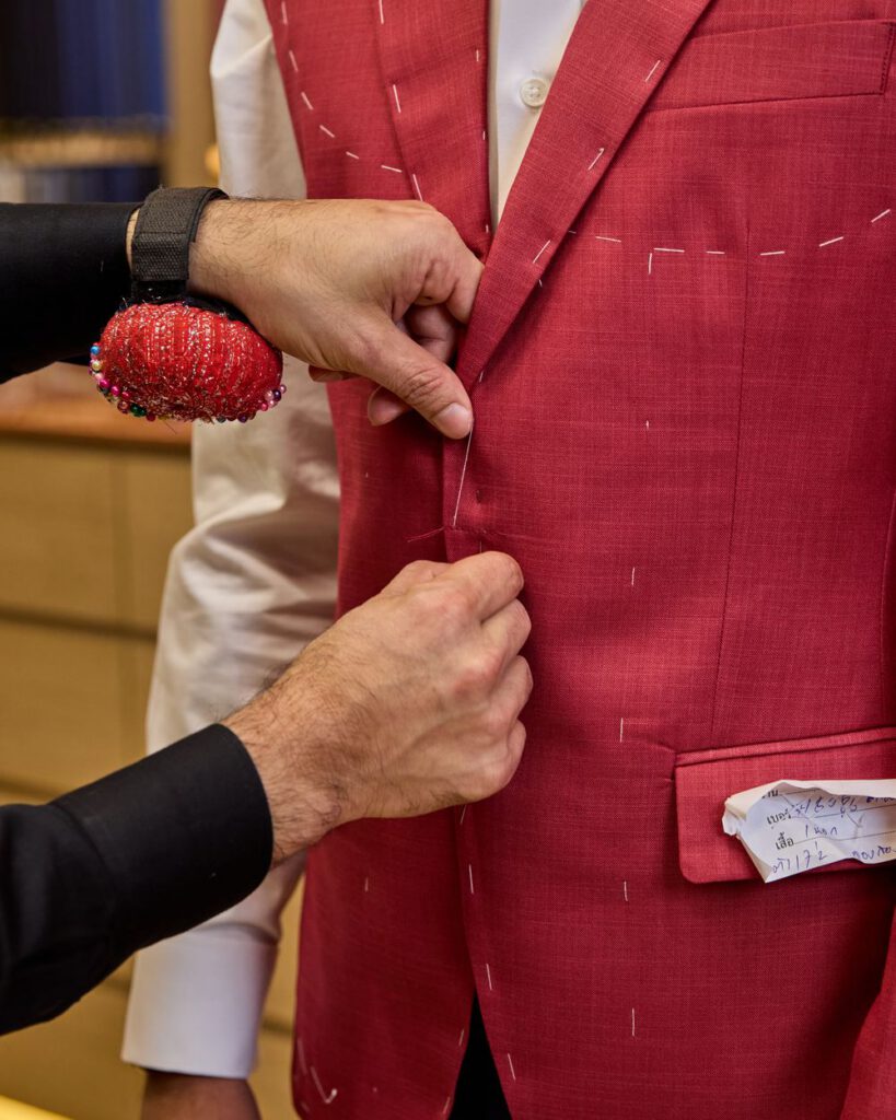 Tailor hand-stitching a red suit jacket during a fitting